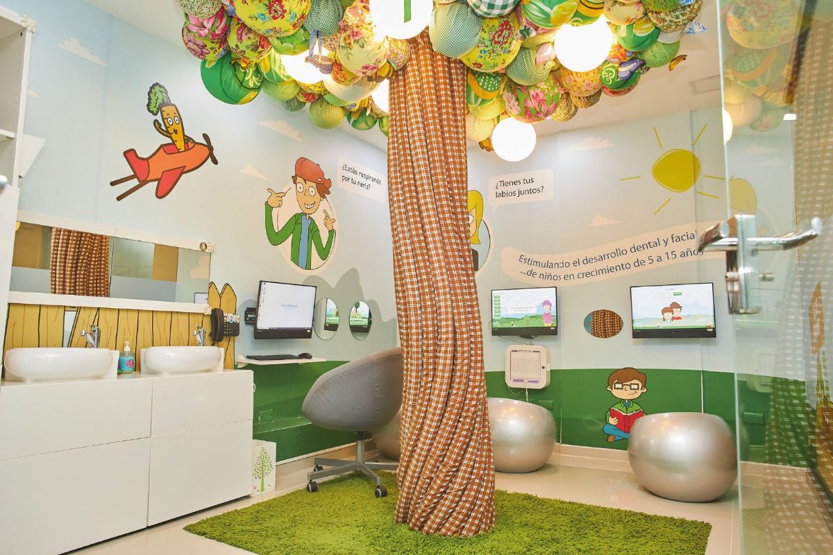 Sala infantil con un árbol de tela en el centro, césped y paredes con dibujos